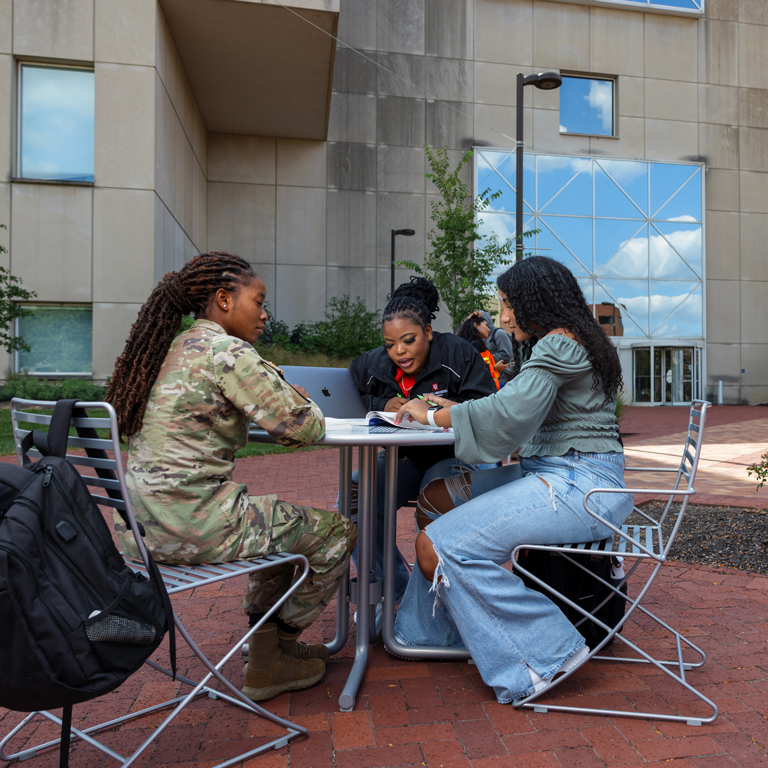 A group of students, one of whom is a soldier, studying in front of the University Library.